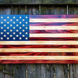 May include: A wooden American flag with red, white, and blue stripes. The flag is made of individual wood planks, each stained a different shade of red, white, or blue. The stars are white and are painted on a blue background.