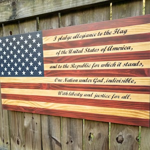 May include: Wooden American flag with the Pledge of Allegiance printed on it. The flag is stained in red, white, and blue.