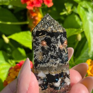 May include: Black, white, and gold crystal point with various inclusions. The crystal is clear and has a pointed top.