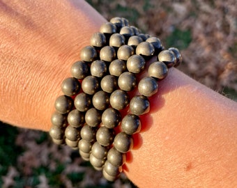 May include: A stack of four gold pyrite beaded bracelets. The beads are round and have a metallic sheen.
