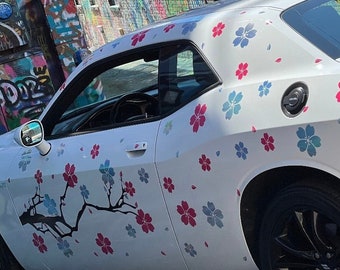 Może przedstawiać: Biały Dodge Challenger z czarnym wzorem wiśni na boku. Samochód ma czarne koła i czarne wnętrze.