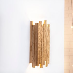 Peut inclure: Une applique murale en bois avec un design g&eacute;om&eacute;trique. L'applique est en bois brun clair et d&eacute;gage une lueur chaude et accueillante.