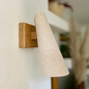 Peut inclure: Un luminaire mural avec une base en bois et un abat-jour en tissu. L'abat-jour est de couleur beige clair et a un tissu texturé.