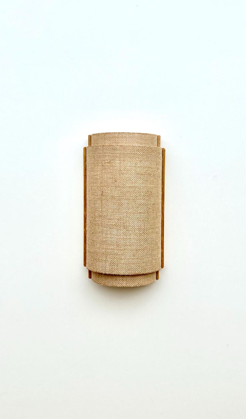 May include: A wall-mounted light fixture with a cylindrical burlap shade and wooden frame.