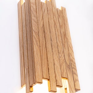 Peut inclure: Une applique murale moderne en lattes de bois naturel. Le luminaire d&eacute;gage une lueur chaude et accueillante.