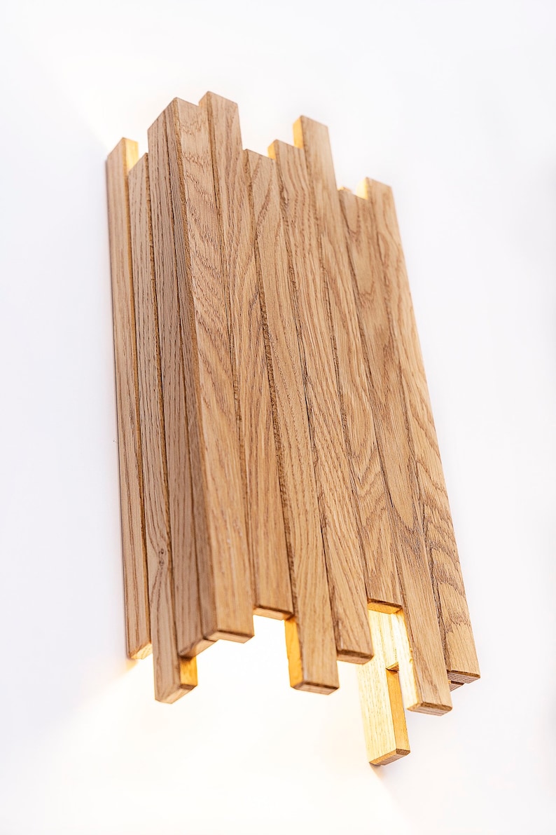 Peut inclure: Une applique murale moderne en lattes de bois naturel. Le luminaire d&eacute;gage une lueur chaude et accueillante.