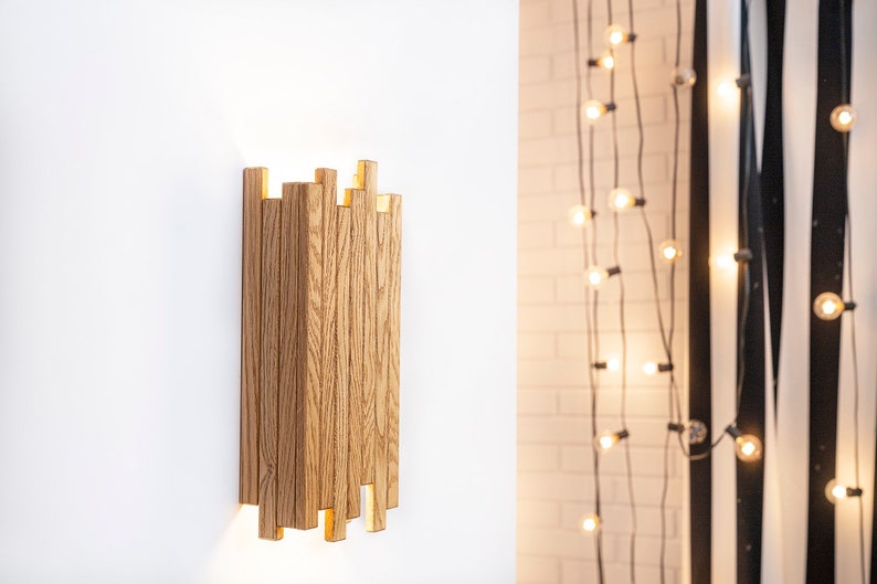 Peut inclure: Une applique murale en bois avec un design g&eacute;om&eacute;trique. L'applique est en bois brun clair et d&eacute;gage une lueur chaude et accueillante.