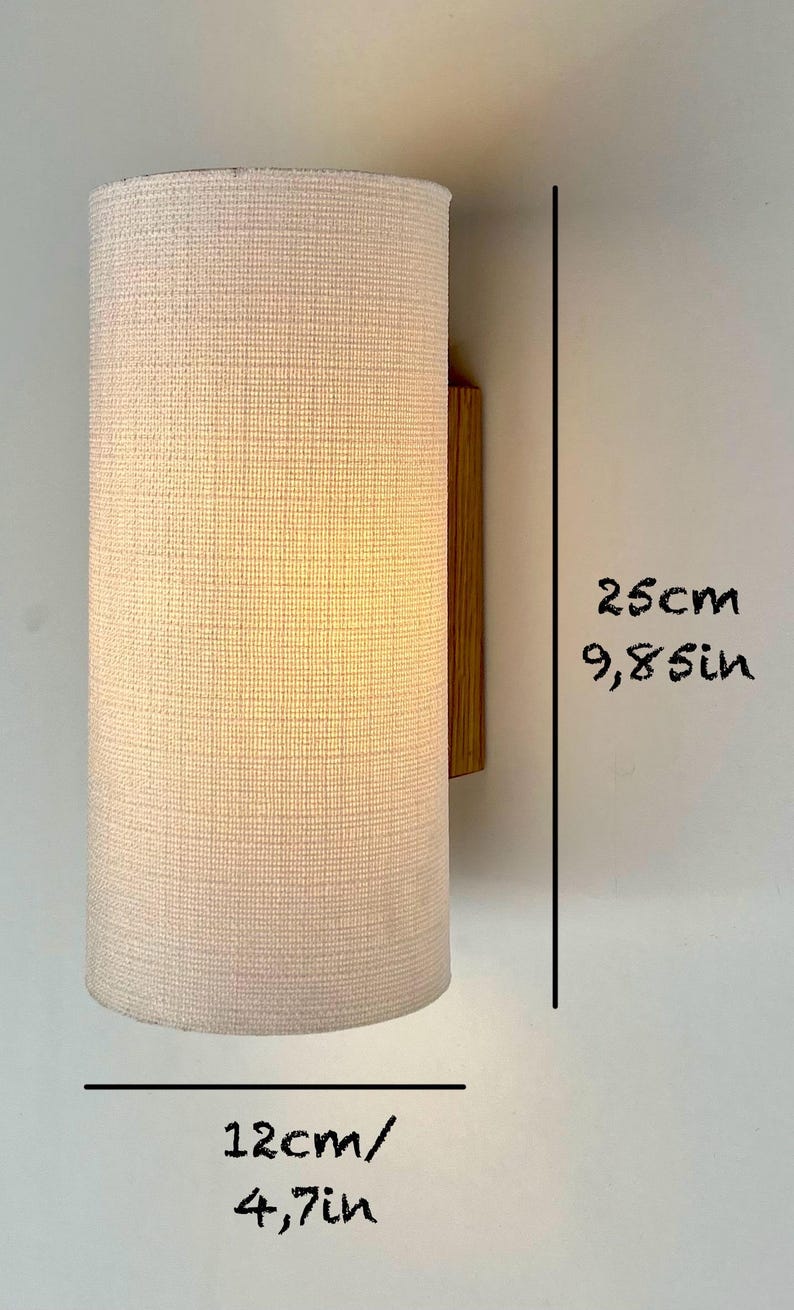 May include: A white fabric cylindrical wall lamp with a wooden base. The lamp is 9.8 inches tall and 4.7 inches wide.