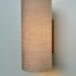 Puede incluir: Aplique de pared cil&iacute;ndrico con pantalla de tela beige. La pantalla tiene un aspecto texturizado y est&aacute; montada sobre una base de madera. El aplique est&aacute; dise&ntilde;ado para iluminaci&oacute;n interior.
