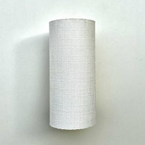 May include: White cylindrical lampshade with a textured fabric surface.