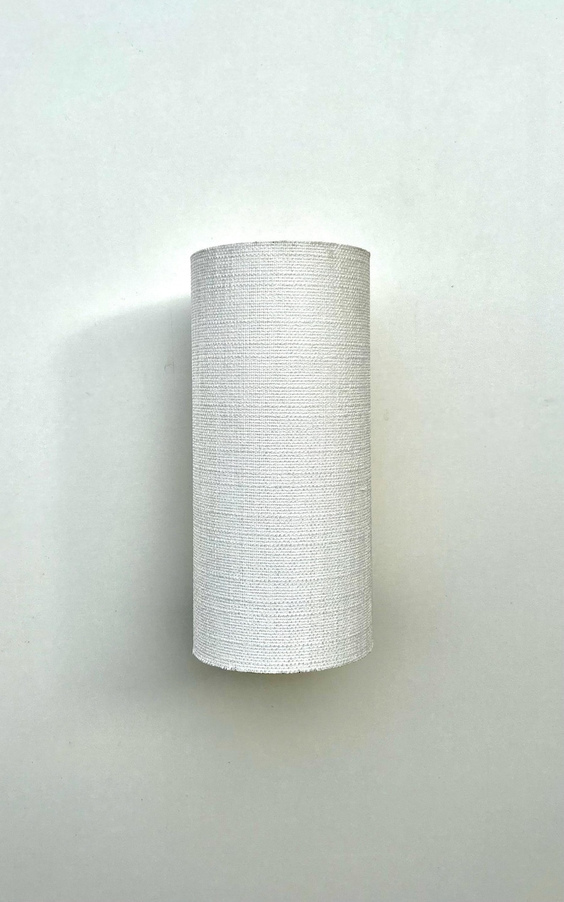 May include: White cylindrical lampshade with a textured fabric surface.