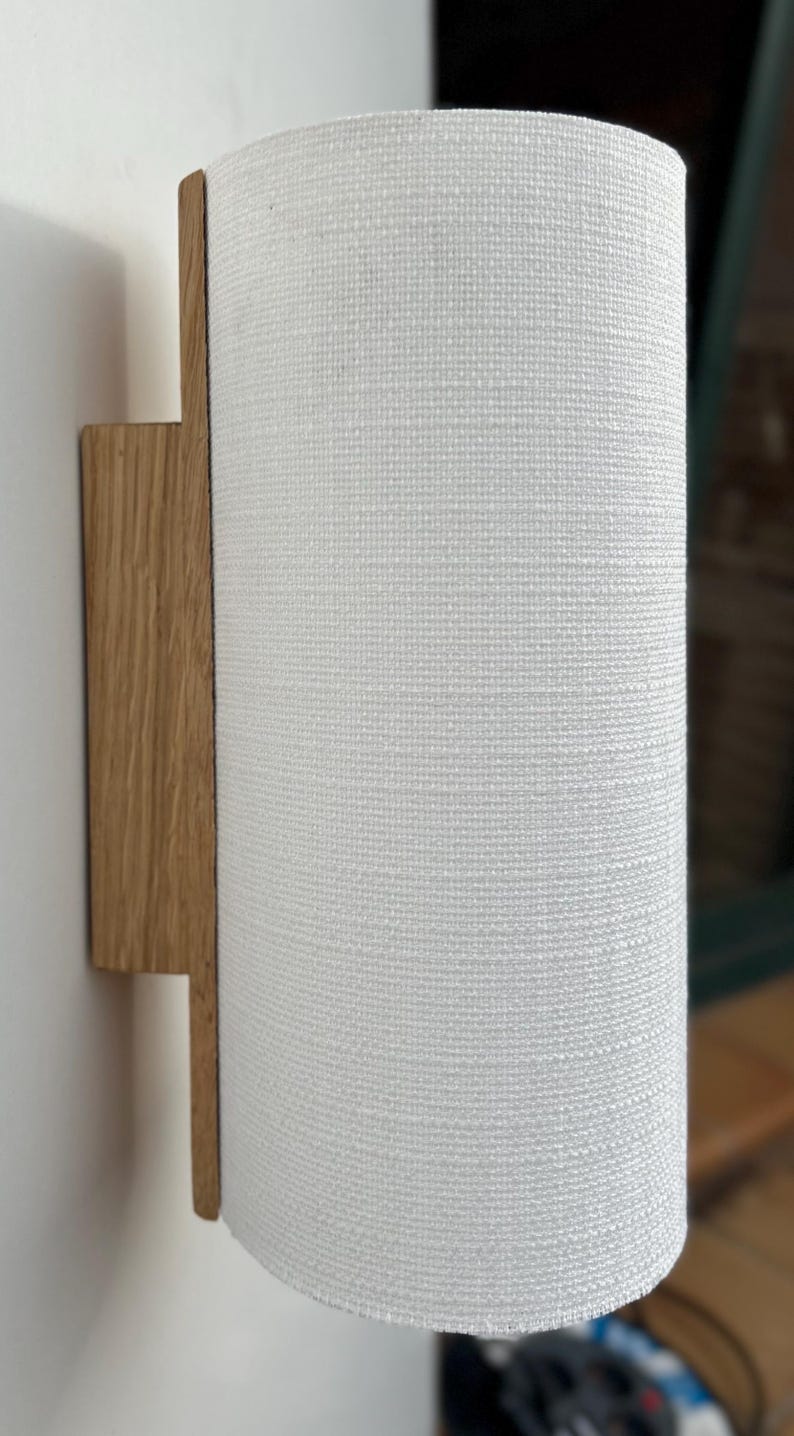 May include: A white fabric cylindrical lampshade attached to a wooden wall sconce.