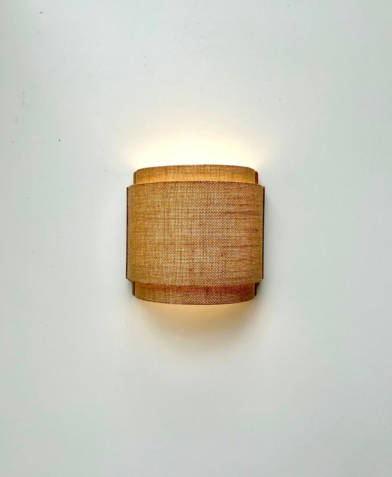 May include: A wall-mounted light fixture with a woven, cylindrical shade. The shade is made of a natural material, like jute or hemp, and has a warm, inviting glow.