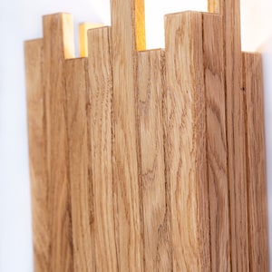 Peut inclure: Un luminaire mural en lattes de bois naturel. Le luminaire a un design moderne et minimaliste et est parfait pour ajouter une touche de chaleur et de texture &agrave; n'importe quelle pi&egrave;ce.
