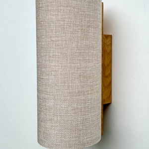 Puede incluir: Aplique de pared cil&iacute;ndrico con pantalla de tela beige y soporte de montaje de madera. La pantalla es de color beige claro y tiene un aspecto texturizado. El soporte de madera es de color marr&oacute;n c&aacute;lido.