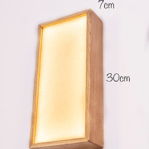Pu&ograve; includere: Un'applique da parete rettangolare in legno con una luce all'interno. L'applique misura 15 cm di larghezza, 7 cm di altezza e 30 cm di lunghezza.