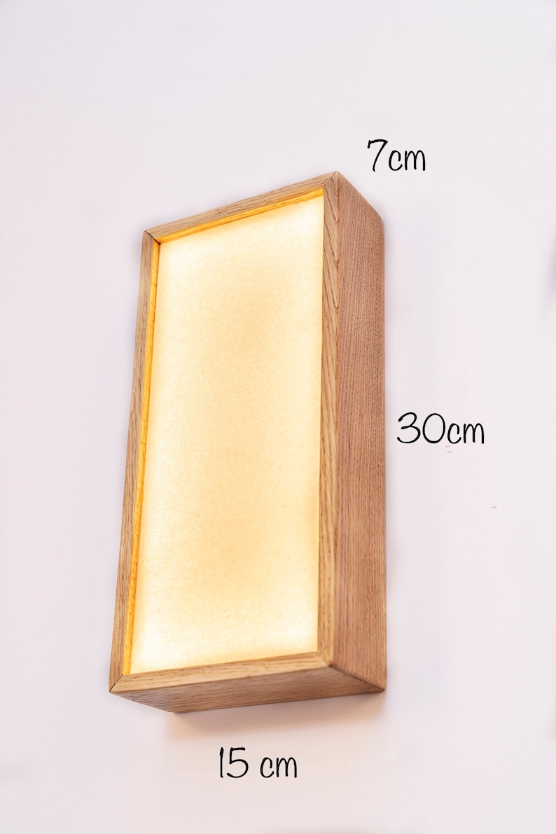 Pu&ograve; includere: Un'applique da parete rettangolare in legno con una luce all'interno. L'applique misura 15 cm di larghezza, 7 cm di altezza e 30 cm di lunghezza.
