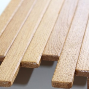 Peut inclure: Gros plan sur un panneau mural en lattes de bois. Les lattes sont dispos&eacute;es en quinconce, cr&eacute;ant une surface textur&eacute;e. Le bois est de couleur brun clair.