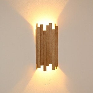 Peut inclure: Une applique murale moderne en bois avec une lumi&egrave;re chaude &eacute;manant du centre.