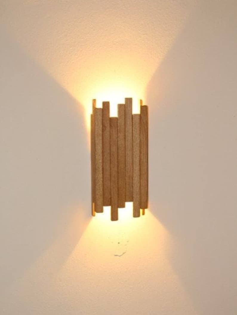 Peut inclure: Une applique murale moderne en bois avec une lumi&egrave;re chaude &eacute;manant du centre.