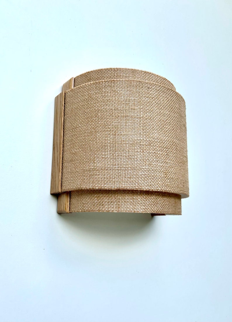 May include: A wall-mounted light fixture with a curved, natural burlap shade and a wooden frame.