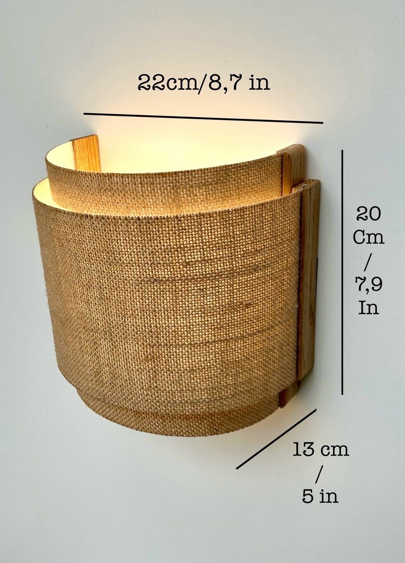 May include: A wall-mounted light fixture with a natural burlap shade and wooden frame. The shade is 7.9 inches tall and 5 inches wide. The fixture is 8.7 inches in diameter.