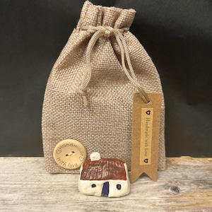 May include: A tan hessian drawstring pouch featuring a round wooden button with the text Handmade with Love and a matching rectangular kraft paper tag with the text Handmade with Love, accompanied by a small ceramic house figurine with a brown roof.