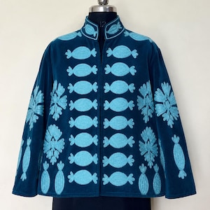 Può includere: Una giacca in velluto blu ottanio scuro con colletto alto e maniche lunghe. Il capo è decorato con motivi ricamati in azzurro, tra cui disegni ripetuti a forma di caramella sul davanti e motivi floreali sui lati e sul colletto.