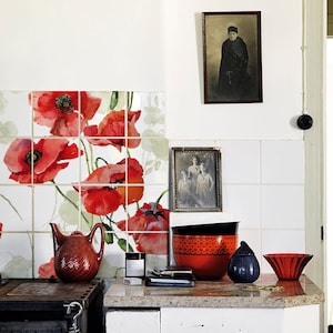 May include: A white tiled kitchen with red poppy floral tile accents. A red and black bowl, a blue teapot, and a red glass bowl are on the counter.