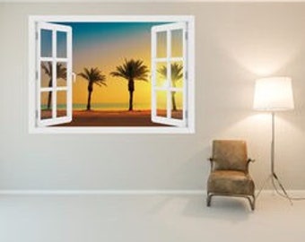 Op de afbeelding: Een muursticker met een raam met uitzicht op een strand bij zonsondergang met drie palmbomen die zich aftekenen tegen de oranje en blauwe lucht.