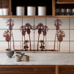 Puede incluir: Una encimera de cocina con una superficie de mármol blanco y gabinetes de madera marrón. El salpicadero es un mural de azulejos de palmeras contra un cielo rosa. Hay cuatro botes de cerámica blanca con tapas de madera en un estante sobre la encimera. También hay cuatro cuencos de cerámica pequeños en la encimera.