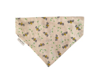 May include: A beige dog bandana with a pattern of yellow bees and green leaves. The bandana has a small white tag that says "Sewgood & Sewbad".