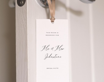 May include: A white rectangular door tag with the text "THIS ROOM IS RESERVED FOR" and "Mr & Mrs Johnstone BRIDAL SUITE" in elegant script. The tag hangs from a silver door handle with a beige ribbon.
