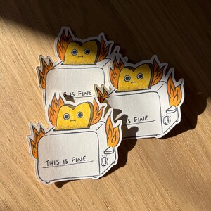 May include: Three white toaster stickers with orange flames and a yellow cartoon toast inside. The text on the stickers reads "This is fine", "This is fine", and "This is fine".