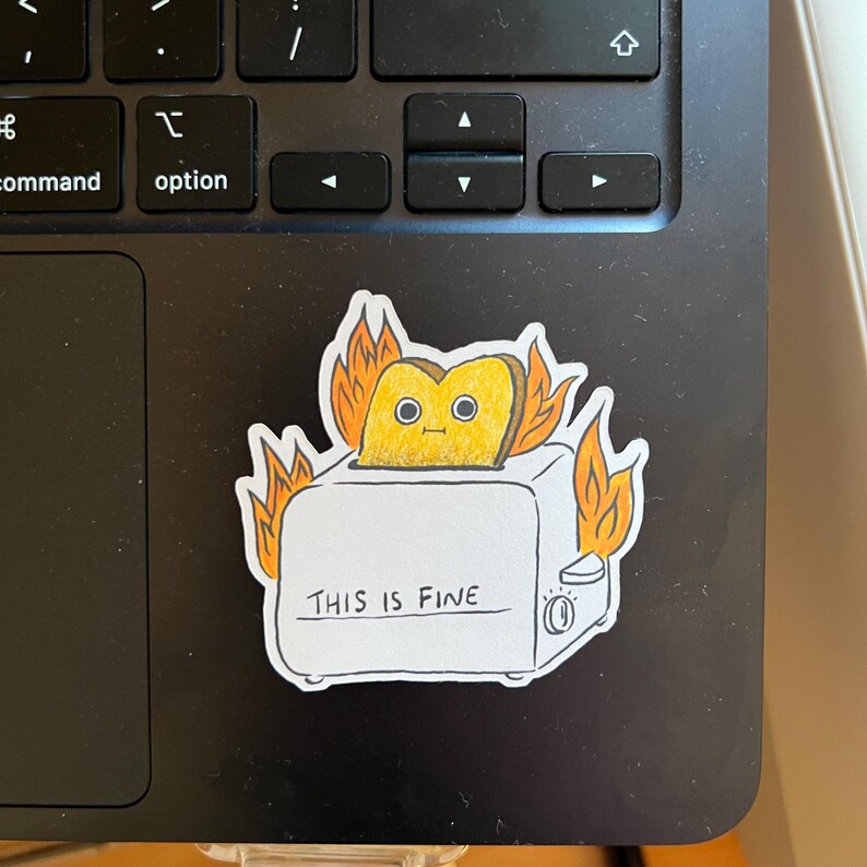 May include: A white toaster with a slice of bread inside, on fire. The toaster has the text "THIS IS FINE" written on it.