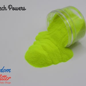 May include: A clear plastic jar tipped over, spilling bright neon yellow glitter onto a white surface. The text "Screech Powers" is above the jar, and the "Freedom Glitter" logo is below.