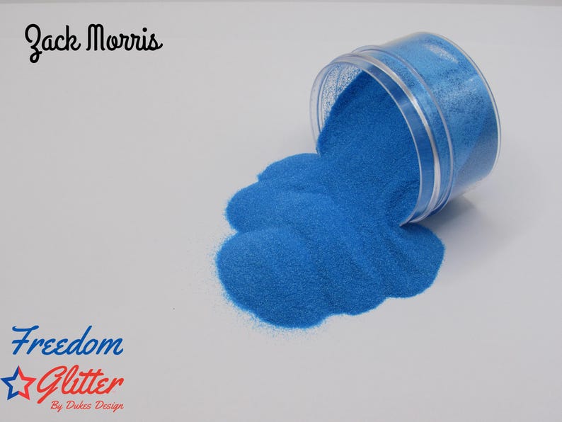 May include: A clear plastic container tipped over, spilling bright blue glitter onto a white surface. The text "Freedom Glitter" and "By Dukes Design" is visible. The name "Zack Morris" is also written in cursive.