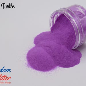 May include: A clear jar tipped over, spilling vibrant purple glitter onto a white surface. The glitter forms a large, textured pile. Text on the image reads "Lisa Turtle" and "Freedom Glitter By Dukes Design".