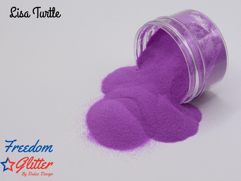 May include: A clear jar tipped over, spilling vibrant purple glitter onto a white surface. The glitter forms a large, textured pile. Text on the image reads "Lisa Turtle" and "Freedom Glitter By Dukes Design".
