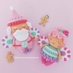 Puede incluir: Dos muñecas de crochet con alas de bastón de caramelo. Las muñecas llevan ropa rosa y verde y tienen los ojos cerrados. Las muñecas están sobre un fondo rosa con galletas de jengibre.