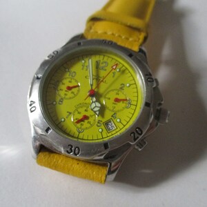 Può includere: Un orologio da polso cronografo giallo con cassa argentata e cinturino in pelle giallo. Il quadrante dell'orologio ha segni neri e accenti rossi.