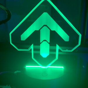 May include: A green illuminated acrylic lamp shaped like an upward arrow. The lamp is on a black base with a white button.