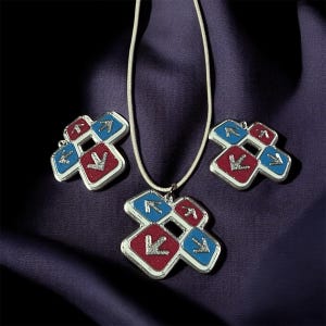 May include: A silver-toned jewelry set featuring a pendant necklace and matching earrings. Each piece has a cross-shaped design with red and blue squares, each with a silver arrow. The set is displayed on a purple fabric.