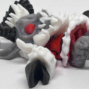 May include: A 3D-printed creature figurine with a detailed design. The figure features a combination of colors, including gray, white, red, and black. The creature has a textured surface and a unique, stylized appearance, possibly a fantasy or sci-fi themed item.
