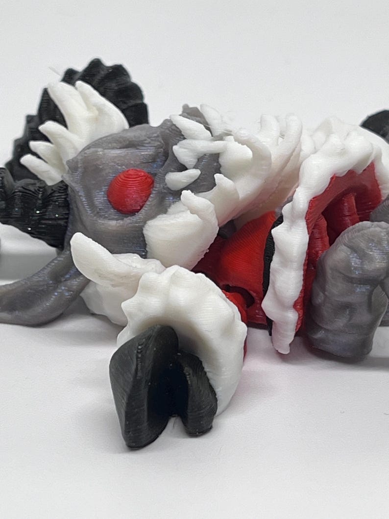 May include: A 3D-printed creature figurine with a detailed design. The figure features a combination of colors, including gray, white, red, and black. The creature has a textured surface and a unique, stylized appearance, possibly a fantasy or sci-fi themed item.