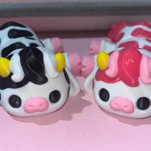 May include: Two small, hand-painted cow figurines. One is black and white, the other is pink and white.