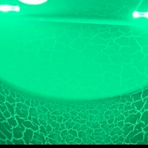 May include: A green cracked glass lamp with a white cord. The lamp is lit and glowing.