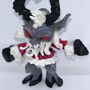 May include: A detailed figurine of a horned creature with red eyes, a gray face, and black horns. The figure has a red and white outfit, with black hooves and hands. The overall design suggests a fantasy or mythological theme.