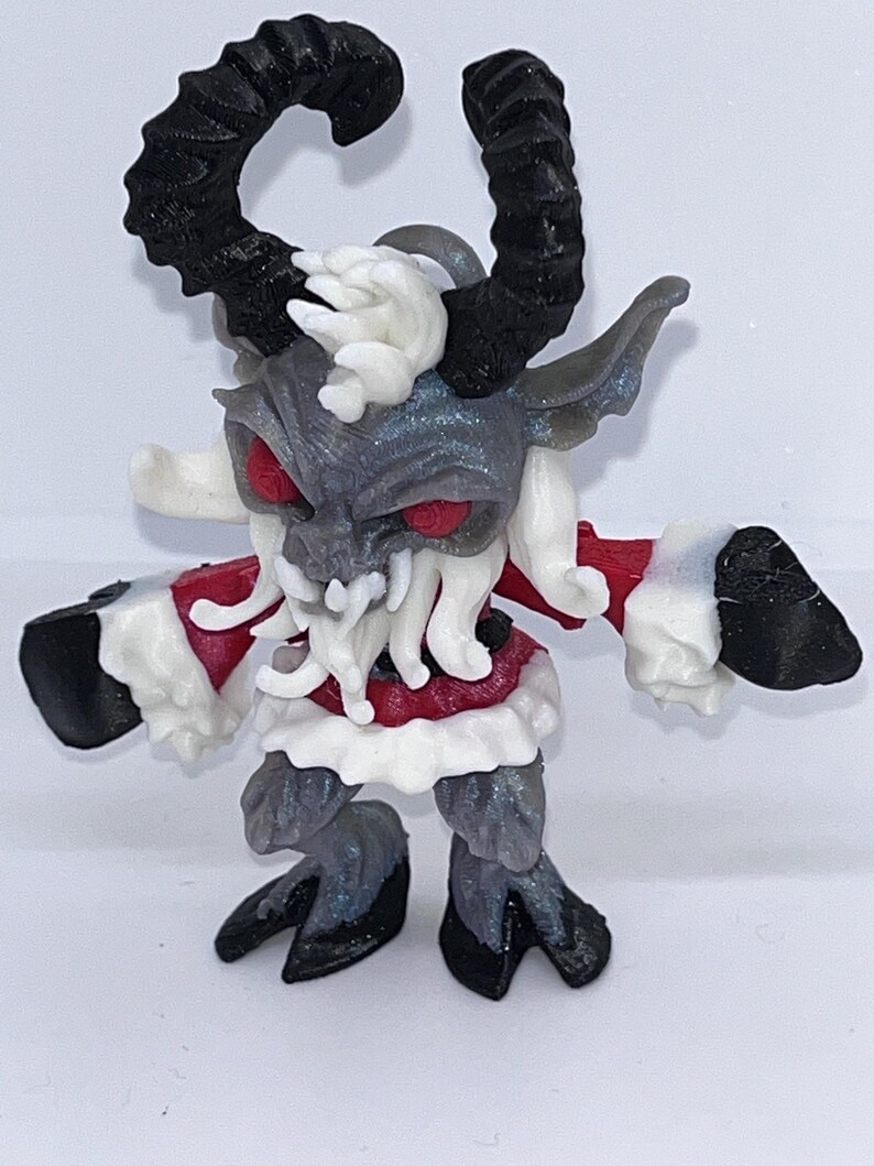May include: A detailed figurine of a horned creature with red eyes, a gray face, and black horns. The figure has a red and white outfit, with black hooves and hands. The overall design suggests a fantasy or mythological theme.