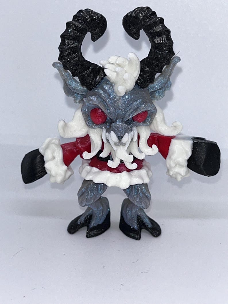 May include: A detailed figurine of a Krampus-like creature. It features large, curved black horns, red eyes, and a menacing expression. The figure is primarily gray with white and red accents, including a red coat with white trim. The feet and hands are black.